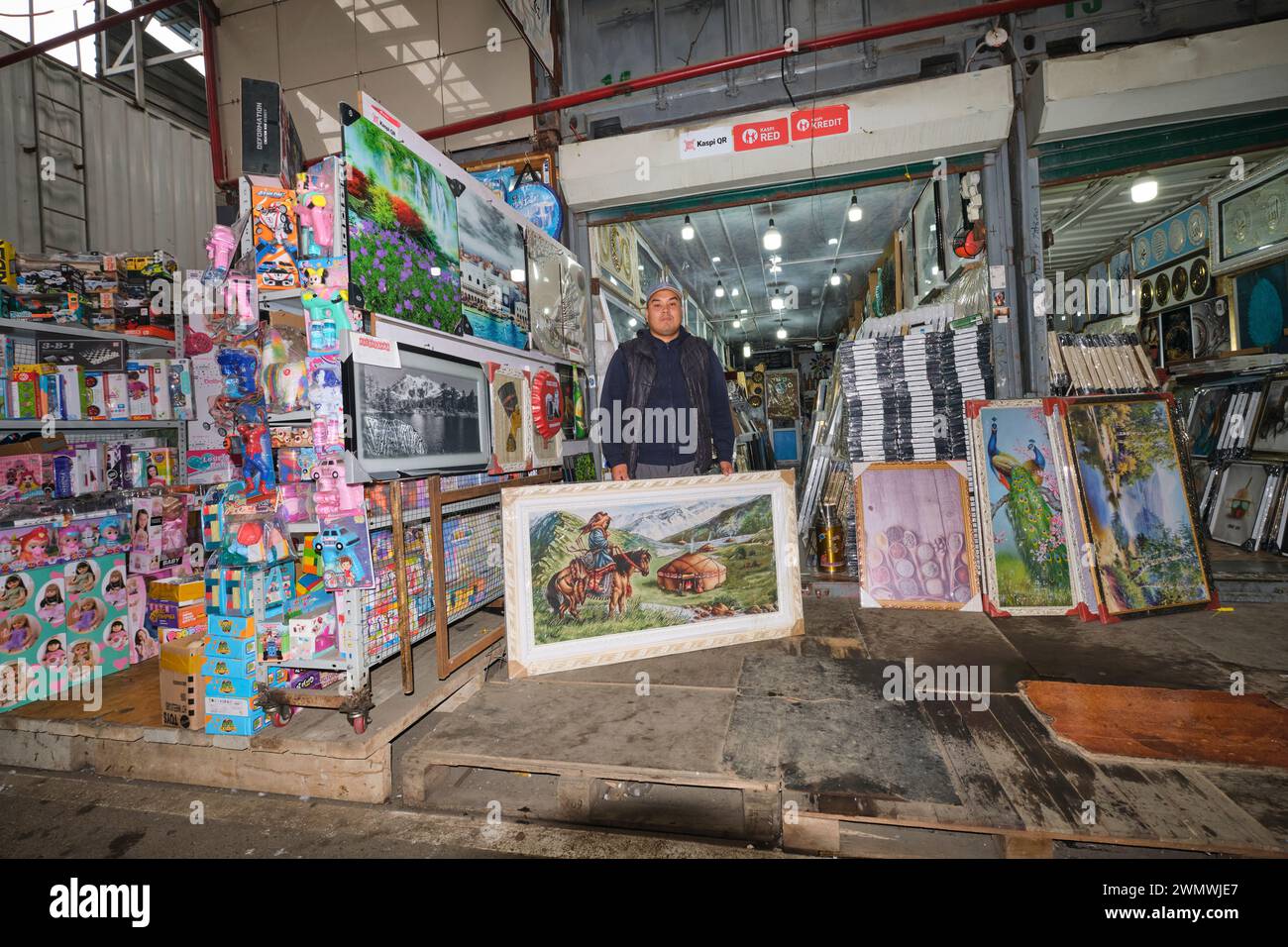 Un ritratto di un venditore, un commerciante con uno dei dipinti, opere d'arte che sta vendendo dal suo negozio. Al mercato locale di Barakholka Shipping Container in Foto Stock