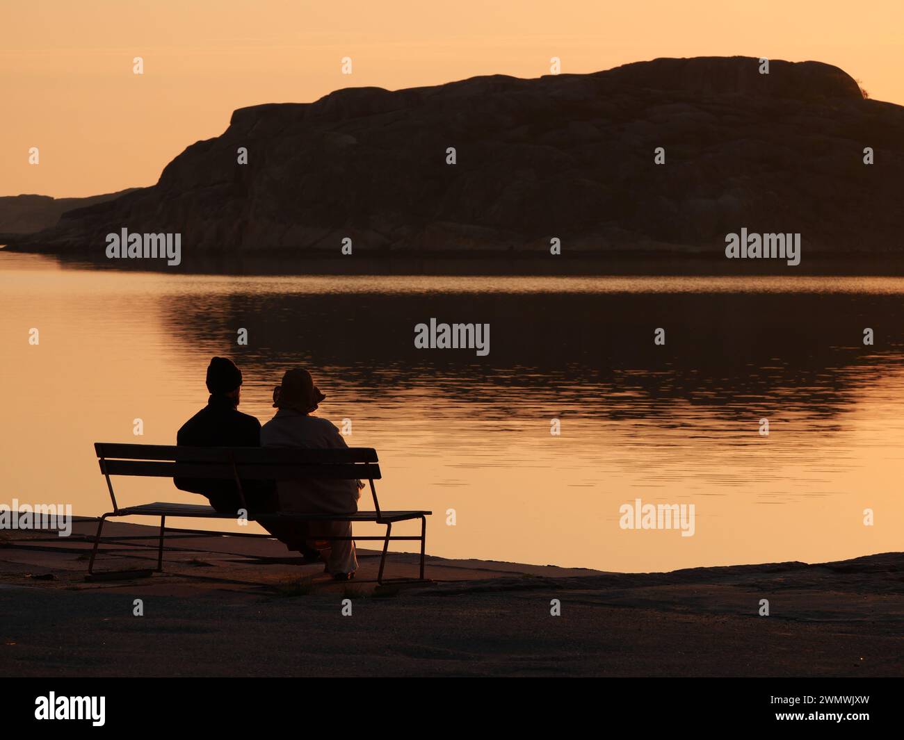 Una coppia seduta su una panchina che guarda il mare al tramonto Foto Stock