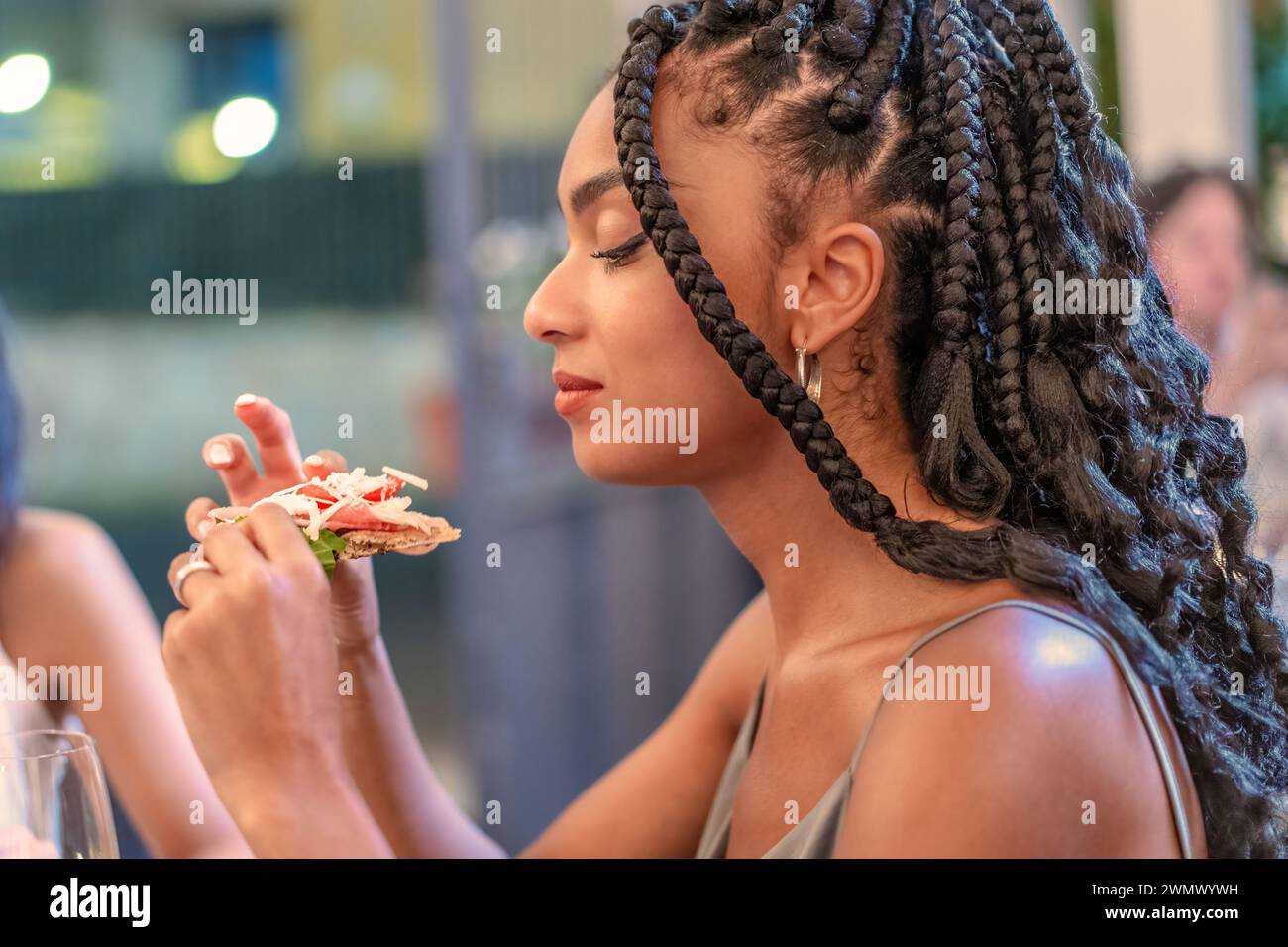 Una giovane donna vizia i ricchi sapori di una pizza italiana gourmet, la sua espressione di un piacere sereno mentre assapora la freschezza e l'alta qualità in Foto Stock