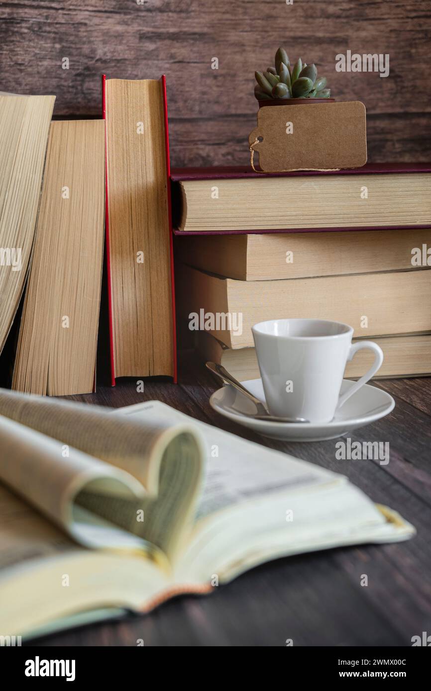 Libro aperto, bicchieri in primo piano, una carta e una tazza di caffè, pile di libri sullo sfondo. Giornata internazionale del libro, cultura, saggezza. Foto Stock