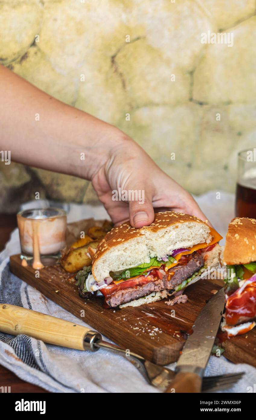 Una mano afferra uno squisito hamburger gourmet tagliato a metà. Sapori irresistibili, concetto di fast food malsano. Foto Stock