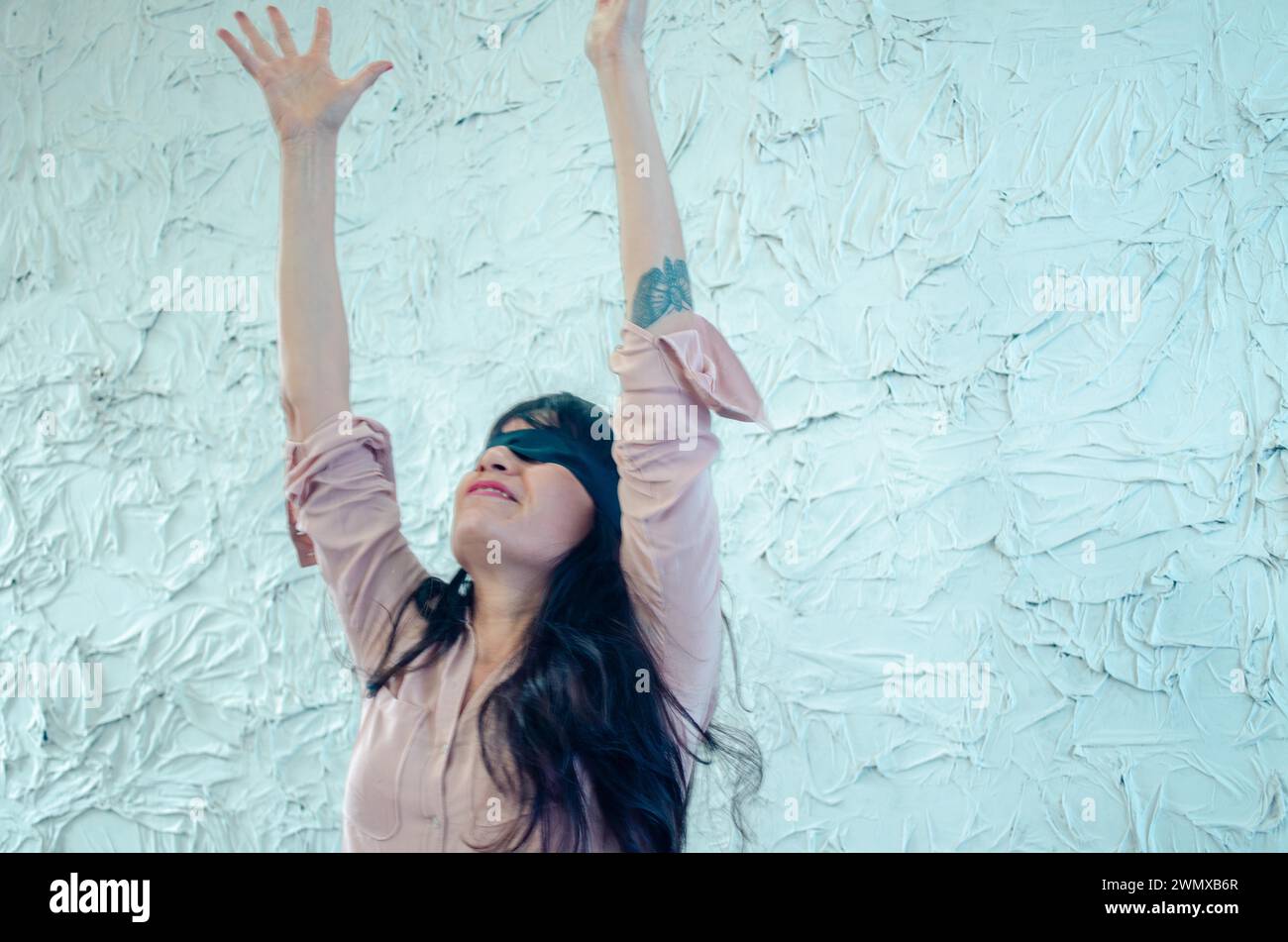 Il movimento dinamico di una giovane donna ispanica giocosa che si avvicina verso l'alto, bendata, contro un muro testurizzato, performance artistiche, giocosa Foto Stock