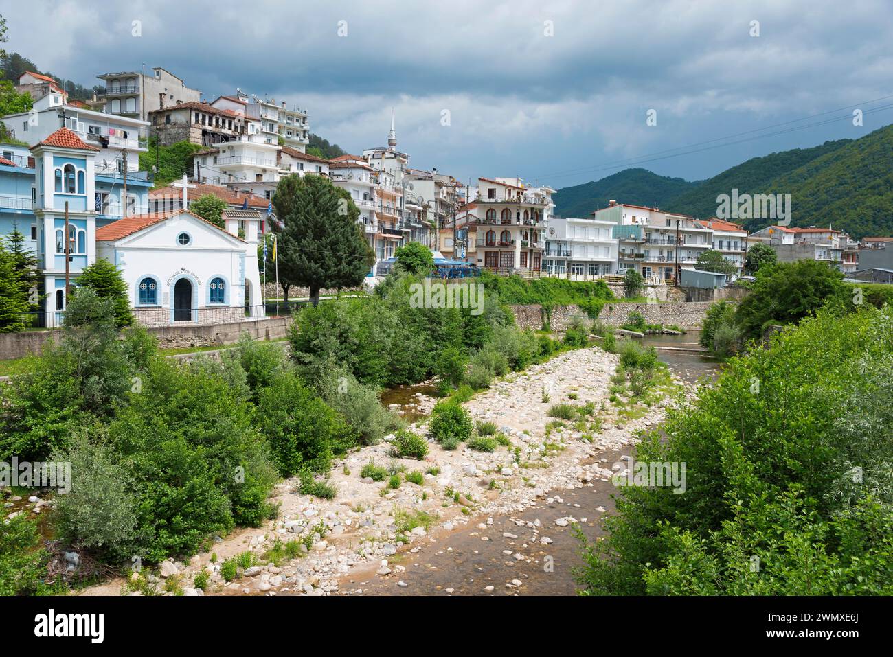 Vista di una piccola città con un fiume in primo piano, circondata da montagne boscose e cielo nuvoloso, Echinos, centro dei Pomaks, Myki, Xanthi Foto Stock