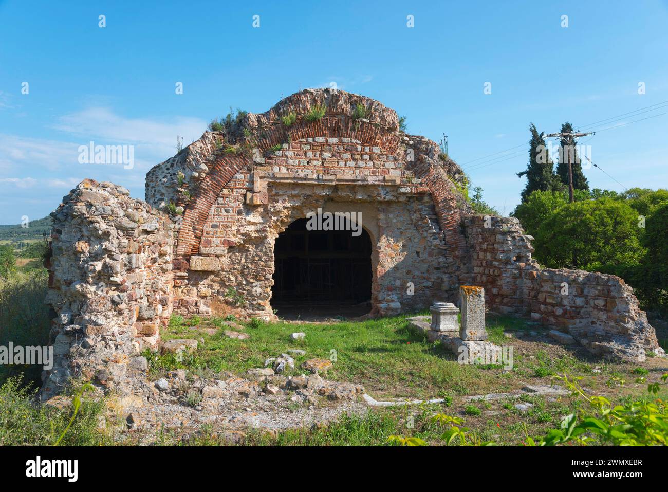Le rovine di un'antica struttura con un arco, circondata da alberi sotto un cielo limpido, sito archeologico di Traianoupolis, Loutra Traianoupoleos Foto Stock