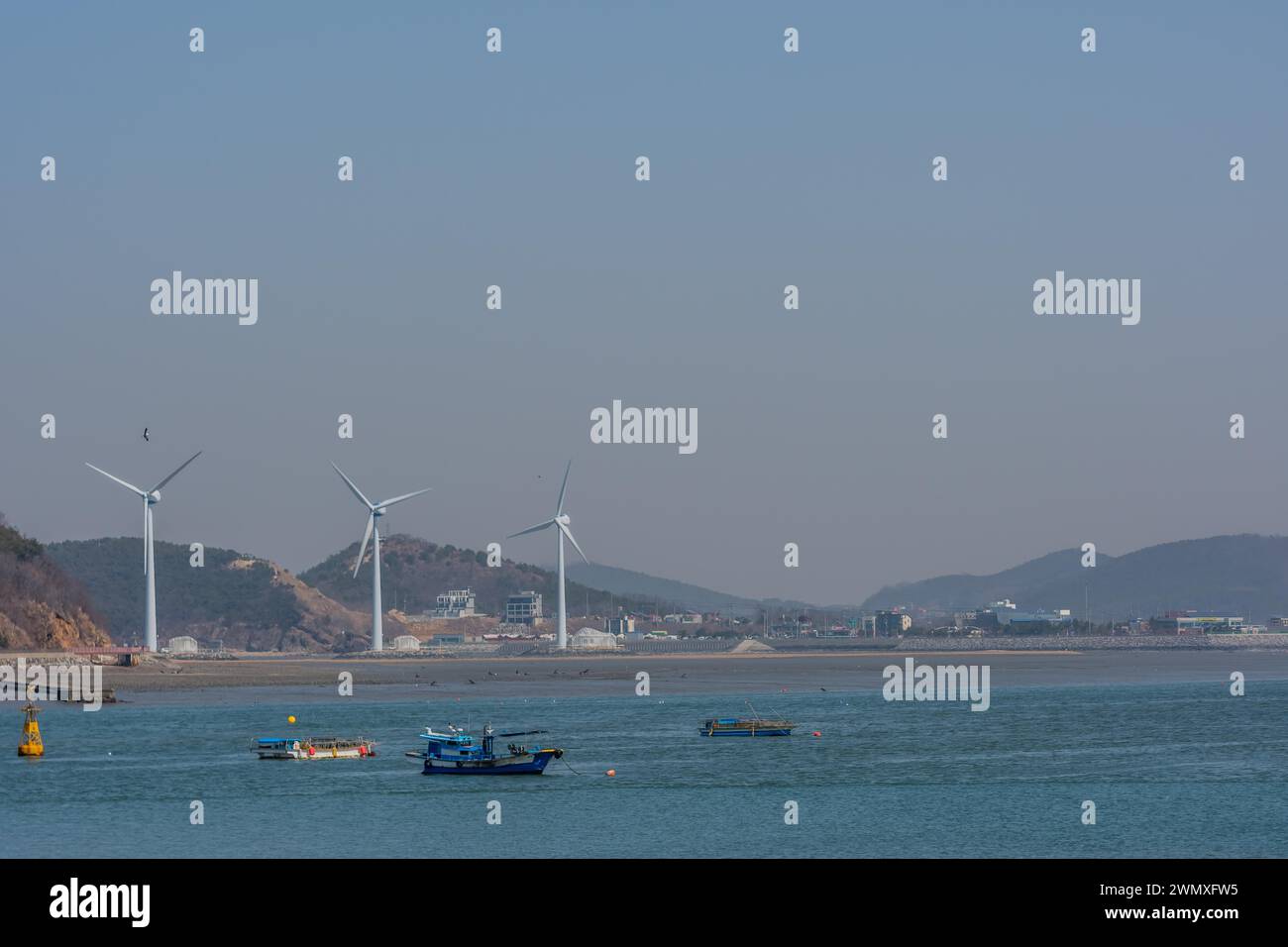Pescherecci da traino ancorati in porto con mulini a vento che generano energia in background a Pyeongtaek, Corea del Sud Foto Stock