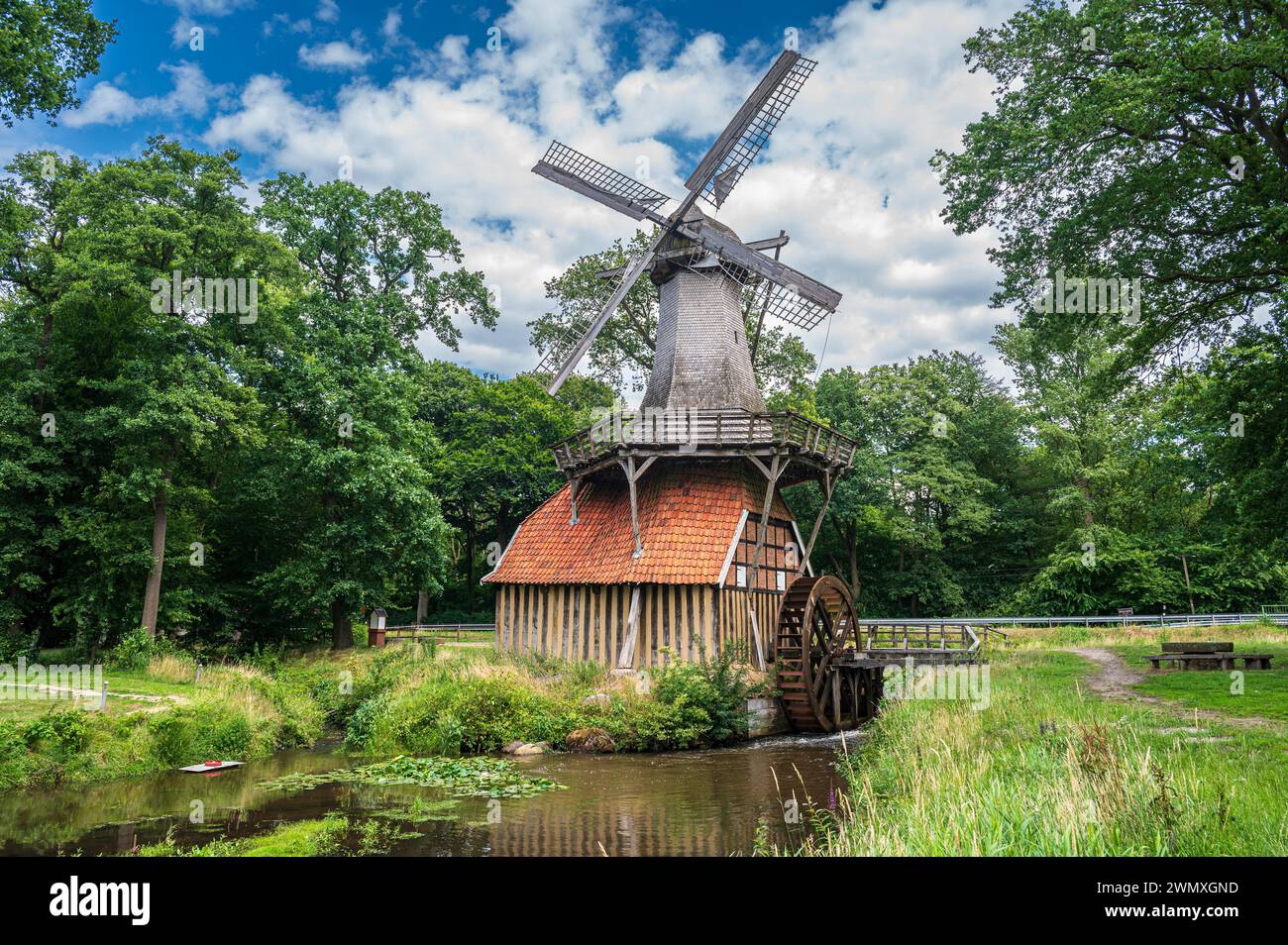 Mulino a vento tradizionale sull'acqua con sfondo boscoso sotto un cielo nuvoloso, Huevener Muehle, Hueven, Emsland, bassa Sassonia Foto Stock