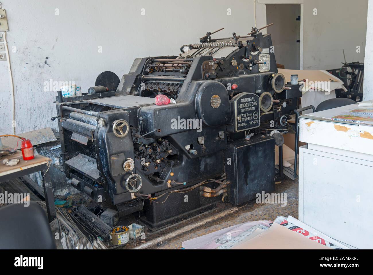 Vecchia macchina da stampa offset in un'officina, circondata da materiali di lavoro, pressa da stampa offset monocolore Heidelberg, Gastouni, Elis, Peloponneso Foto Stock