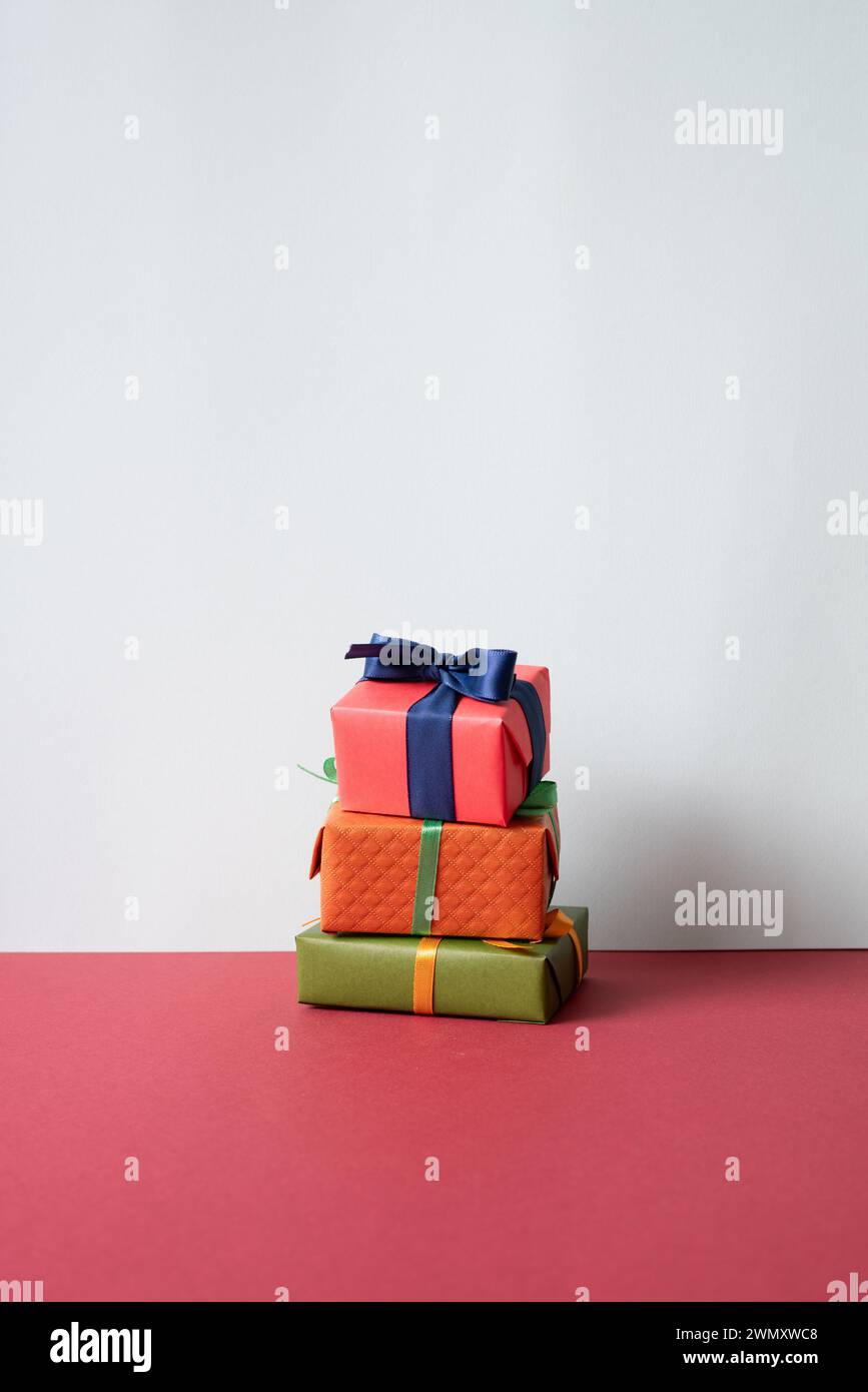 Una pila di confezioni regalo sulla scrivania rossa. sfondo grigio della parete Foto Stock