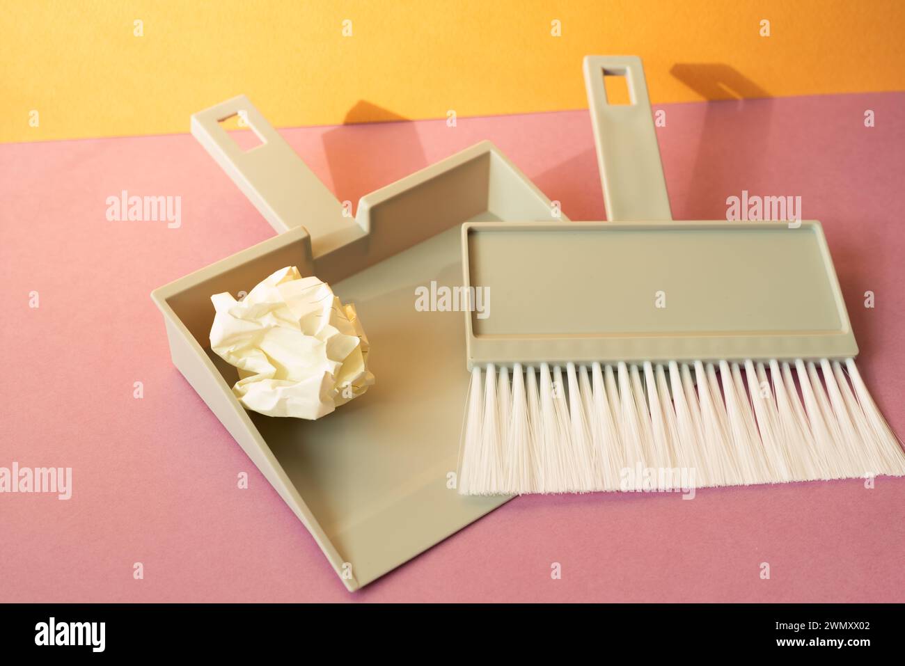 Spazzola in plastica grigia con paletta su pavimento rosa. sfondo arancione della parete Foto Stock