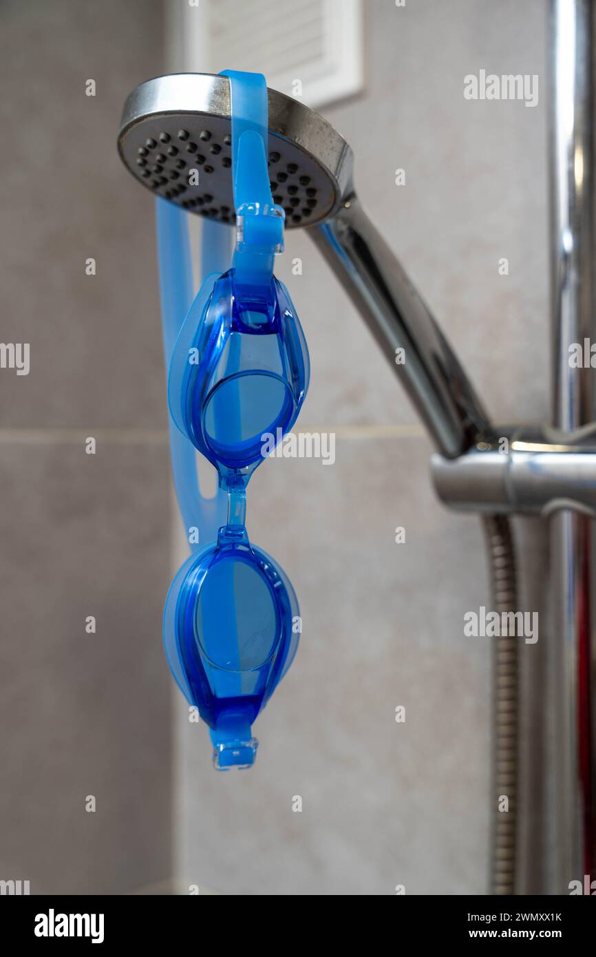 Gli occhiali da bagno sono rimasti appesi nella cabina doccia dopo una nuotata rinfrescante in piscina. Gli occhiali sono appoggiati su un gancio, con gocce d'acqua ancora visibili Foto Stock