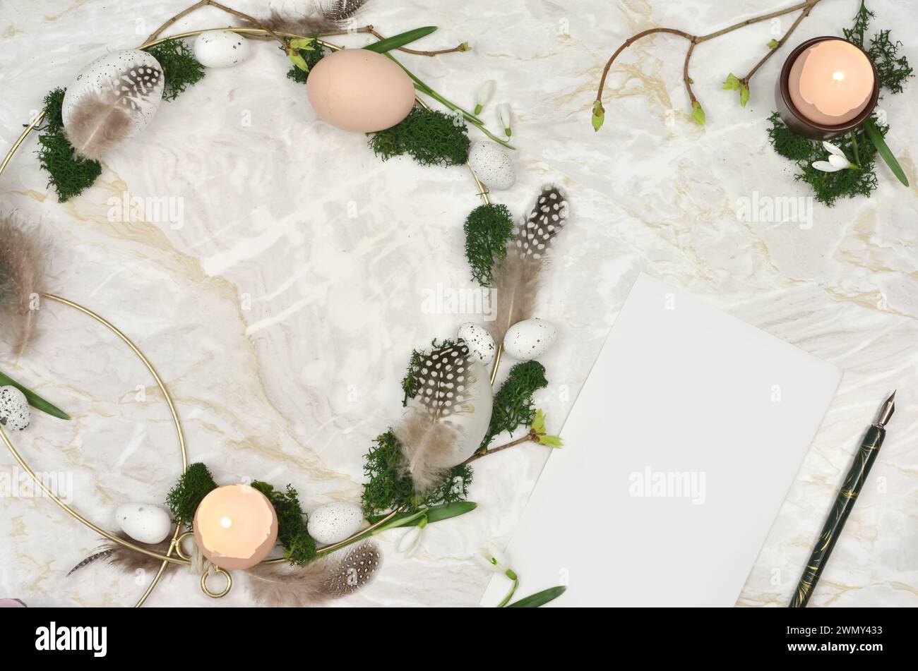 Corona di Pasqua fatta a mano su un tavolo di marmo con foglio di carta bianco da riempire. Uova, gusci d'uovo, candele, muschio - vista dall'alto. Foto Stock
