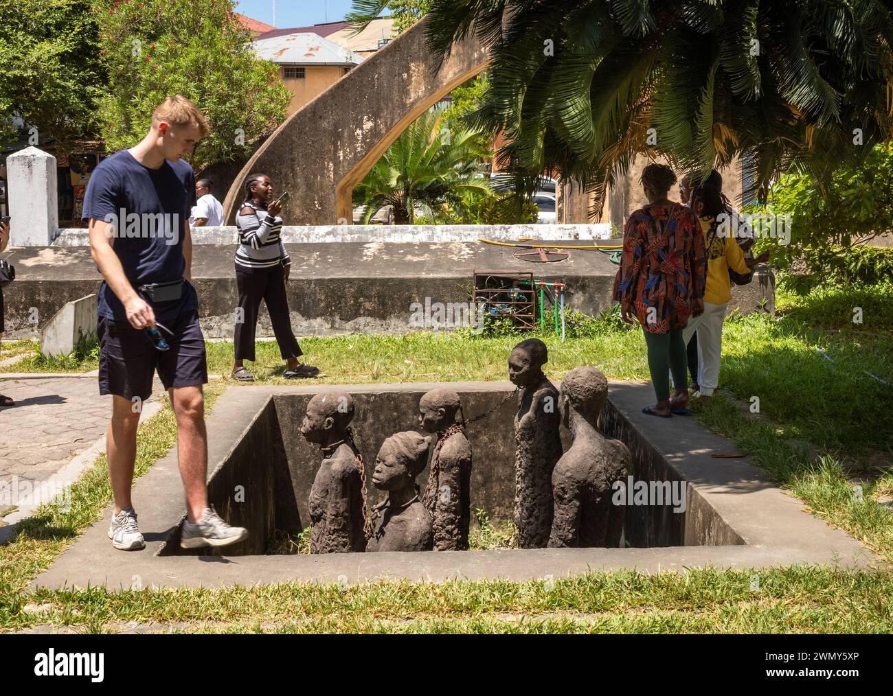 Un turista occidentale visita la scultura commemorativa degli schiavi al vecchio mercato degli schiavi, Stone Town, Zanzibar, Tanzania Foto Stock