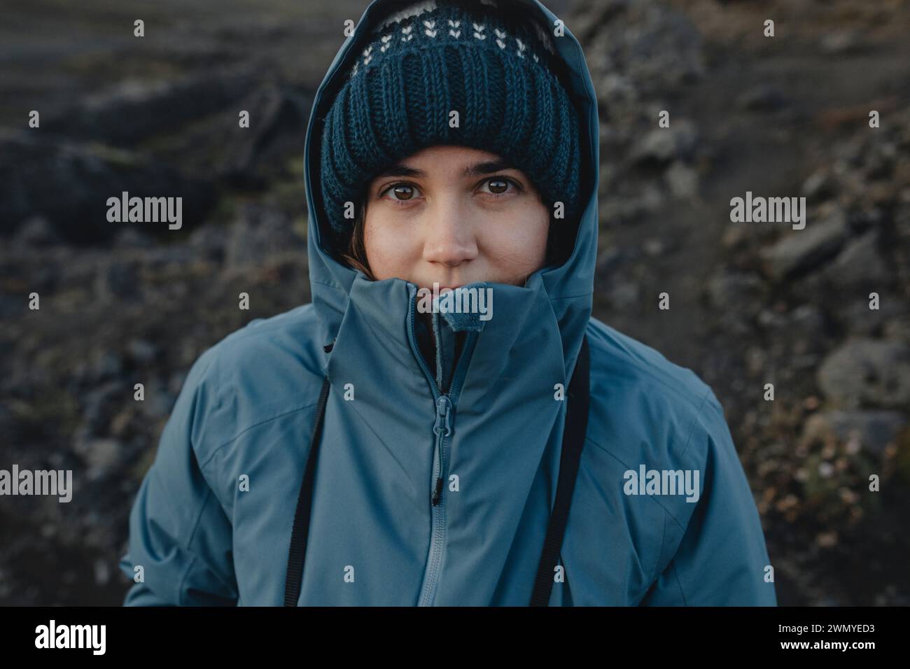 Una donna con giacca blu e berretto guarda la fotocamera con un sorriso sottile in un ambiente islandese. Foto Stock