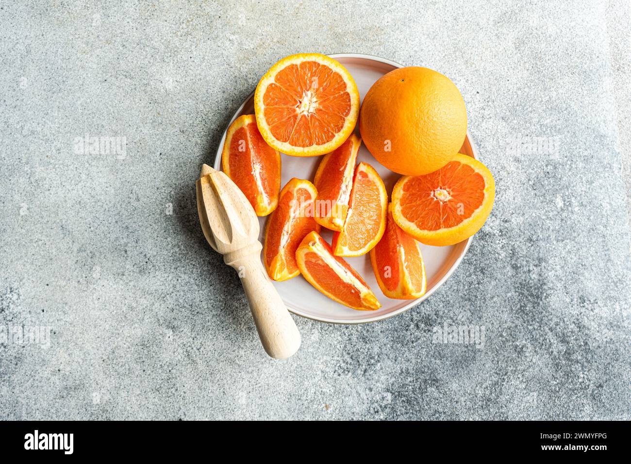 Dal piatto superiore con segmenti di arance mature e un'arancia intera accanto a una centrifuga di agrumi in legno su sfondo testurizzato. Foto Stock