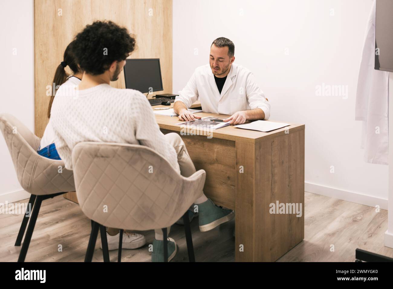 Un medico esamina una pellicola radiografica mentre discute i risultati con un paziente concentrato durante una consultazione in un ufficio clinico. Foto Stock