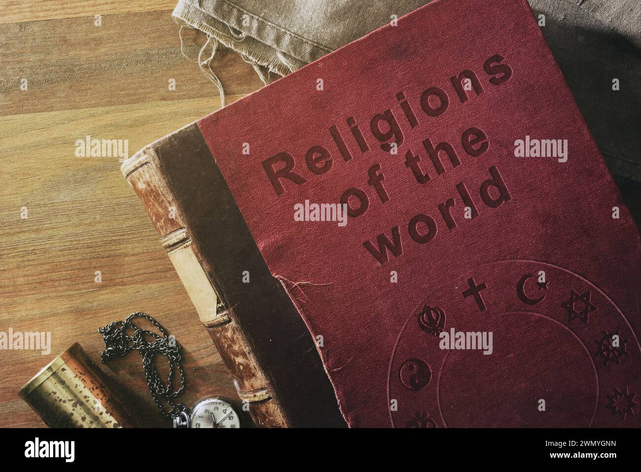 Dettaglio di un vecchio libro sullo studio delle religioni nel mondo con testo inciso e simboli di varie religioni su tavola in legno con oggetti decorativi. Foto Stock