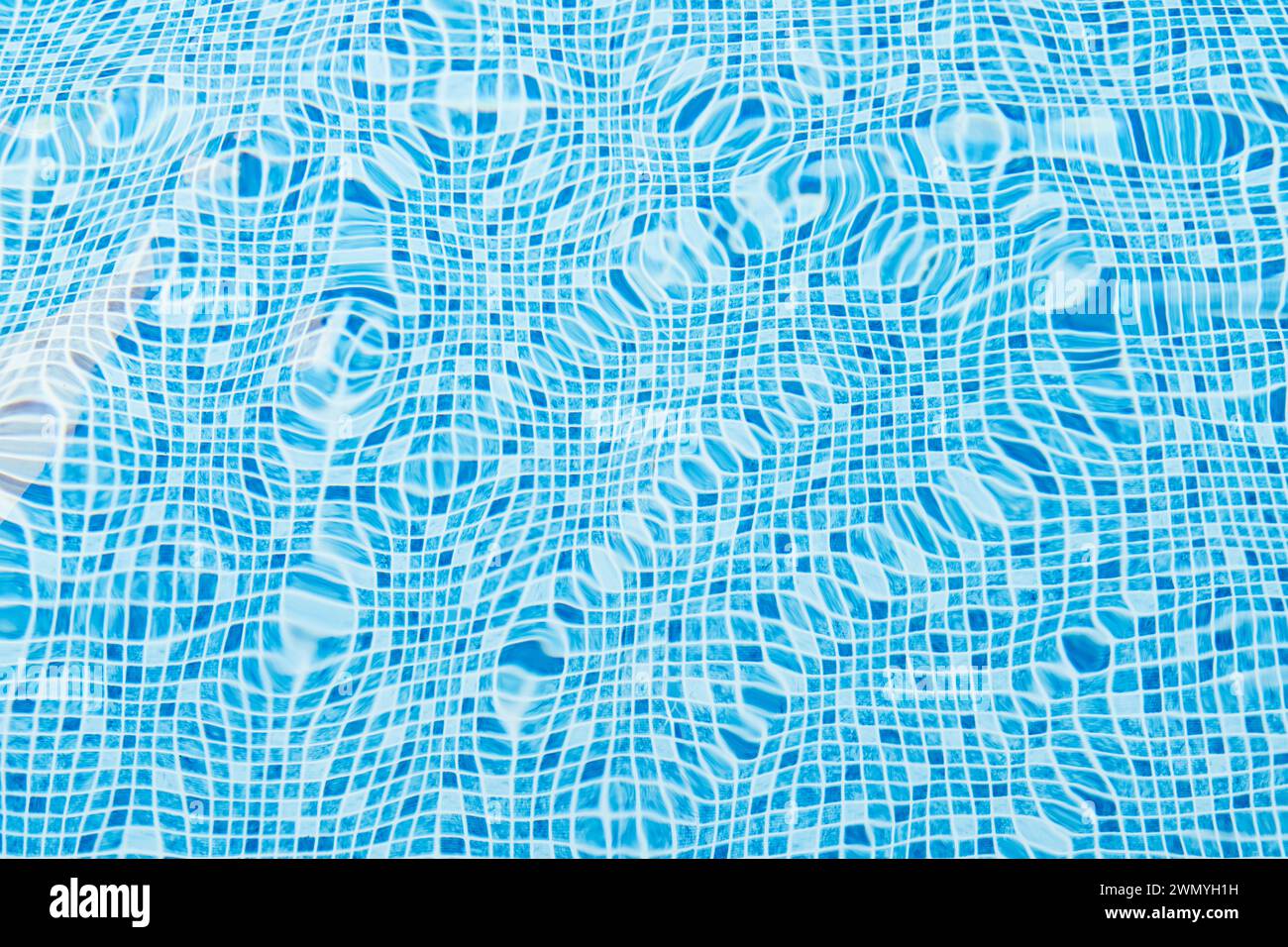 Un primo piano di luce che si riflette sulla superficie ondulata dell'acqua in una piscina fiancheggiata da piastrelle blu brillante Foto Stock