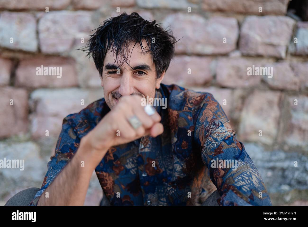 Un giovane gioioso puzza giocosamente l'aria, mostrando un sorriso affascinante e uno stile informale in un ambiente all'aperto Foto Stock