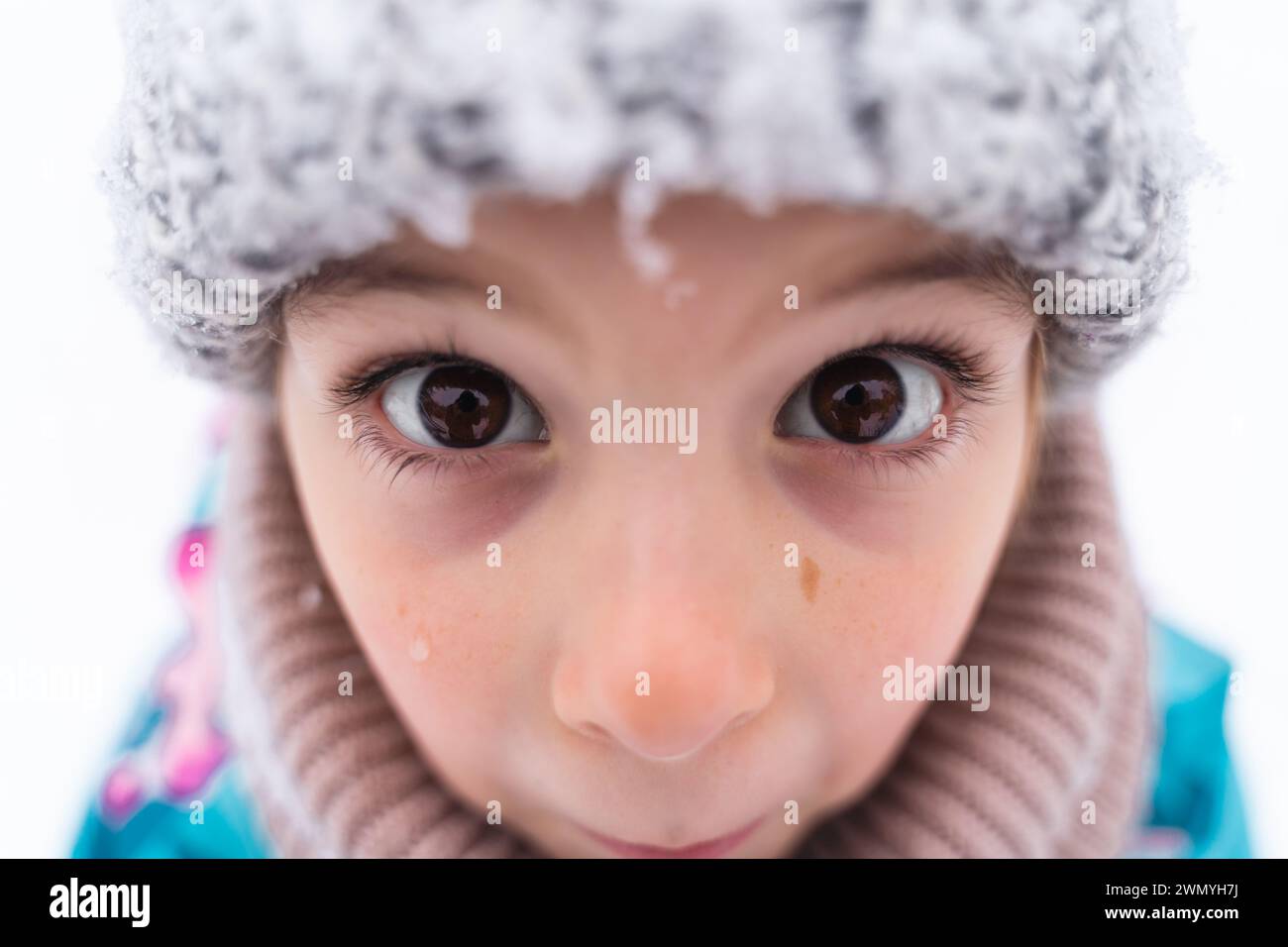 Primo piano degli occhi di un bambino che guarda in alto, indossando un cappello di lana in un ambiente innevato Foto Stock