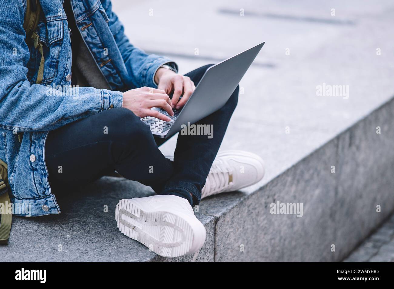 Un giovane anonimo lavora sul suo portatile mentre è seduto sui gradini di una vivace piazza di Madrid Foto Stock