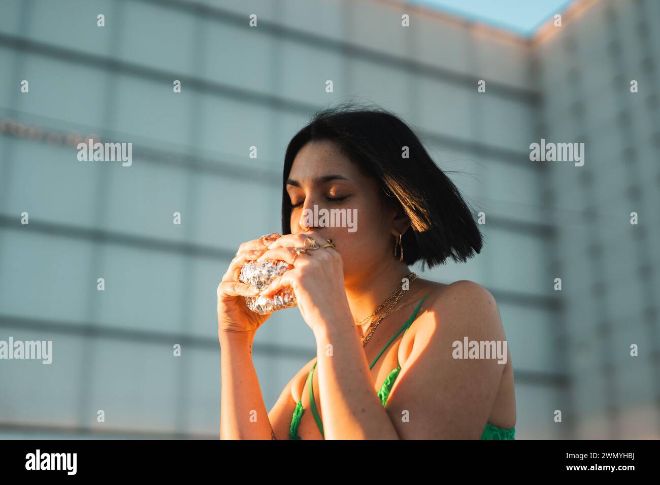 Una donna elegante sorseggia l'acqua da una bottiglia di vetro sullo sfondo moderno della zona affari delle quattro Torri di Madrid. Foto Stock