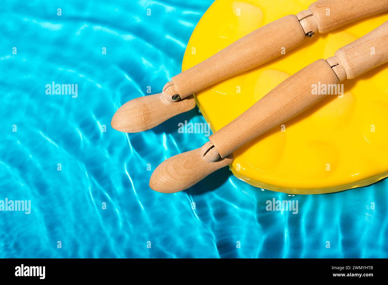 Parte del corpo di una figura di manichino in legno che prende il sole su una piscina gialla galleggiante nell'acqua cristallina della piscina Foto Stock