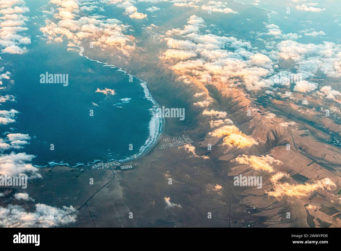 Caleta de Famara e la Bahia de Penedo sull'isola delle Canarie di Lanzarote, in Spagna, viste da un aereo di passaggio verso il tramonto. Foto Stock