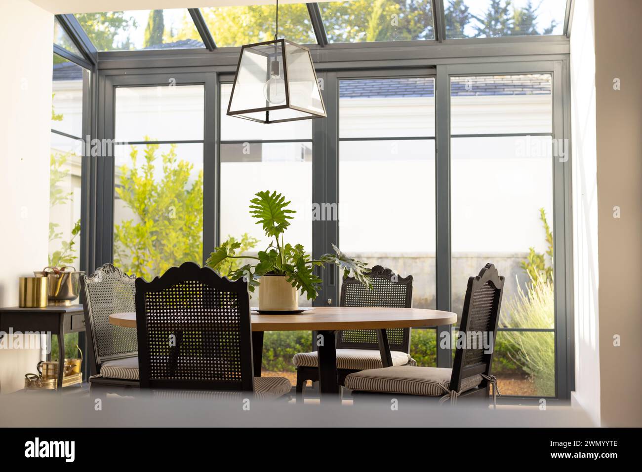 Un'area da pranzo illuminata dal sole a casa presenta un tavolo, sedie e una lampada sospesa Foto Stock