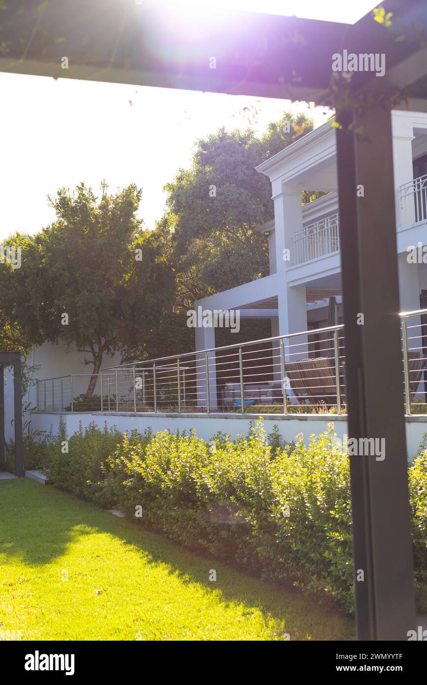 La luce solare filtra attraverso un giardino con una casa bianca sullo sfondo, con spazio per le copie Foto Stock