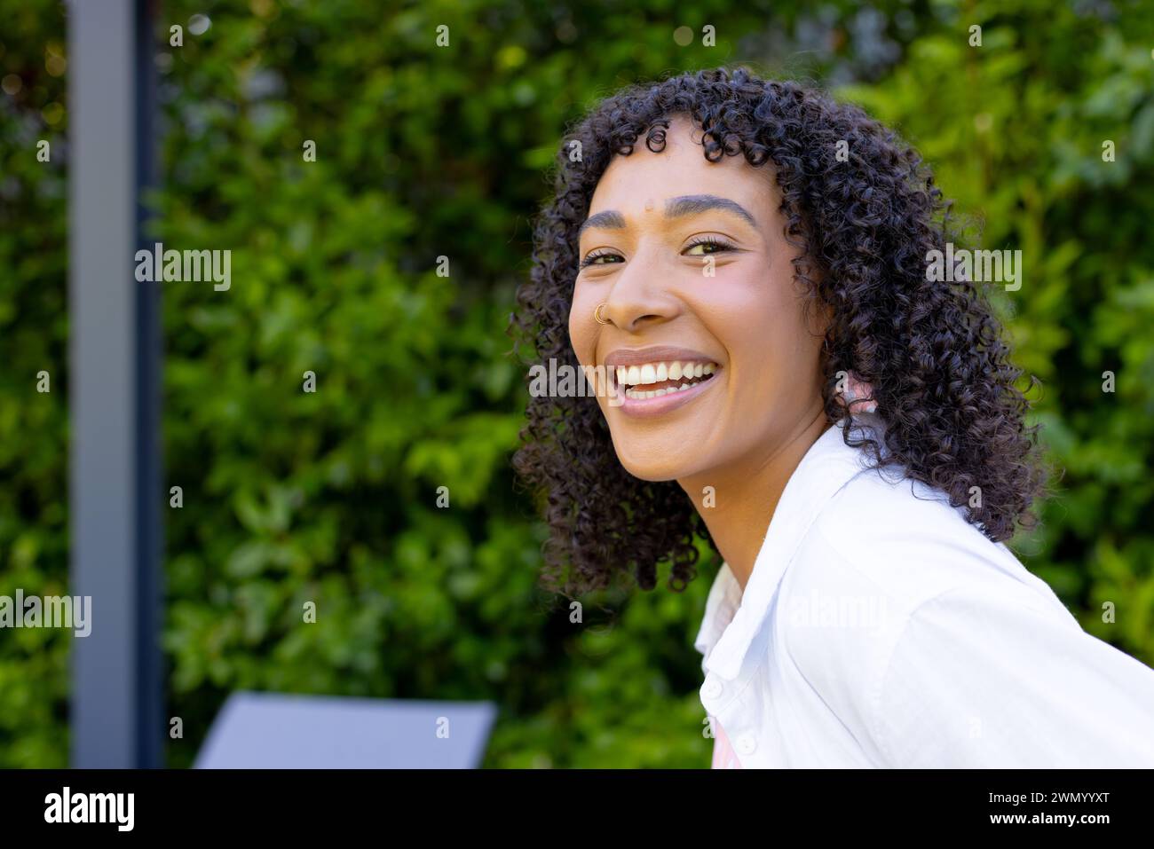 Giovane donna birazziale con capelli neri ricci sorride brillantemente all'aperto a casa con spazio per le copie Foto Stock