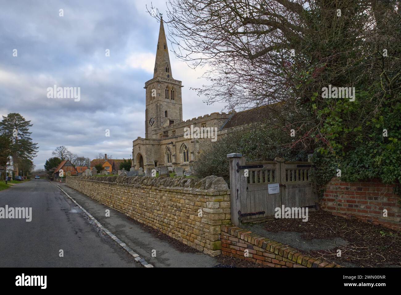 Swineshead, Bedfordshire, Inghilterra, Regno Unito - Chiesa di San Nicola con il suo muro di pietra che circonda il cimitero, una chiesa anglicana nel villaggio di High Street Foto Stock