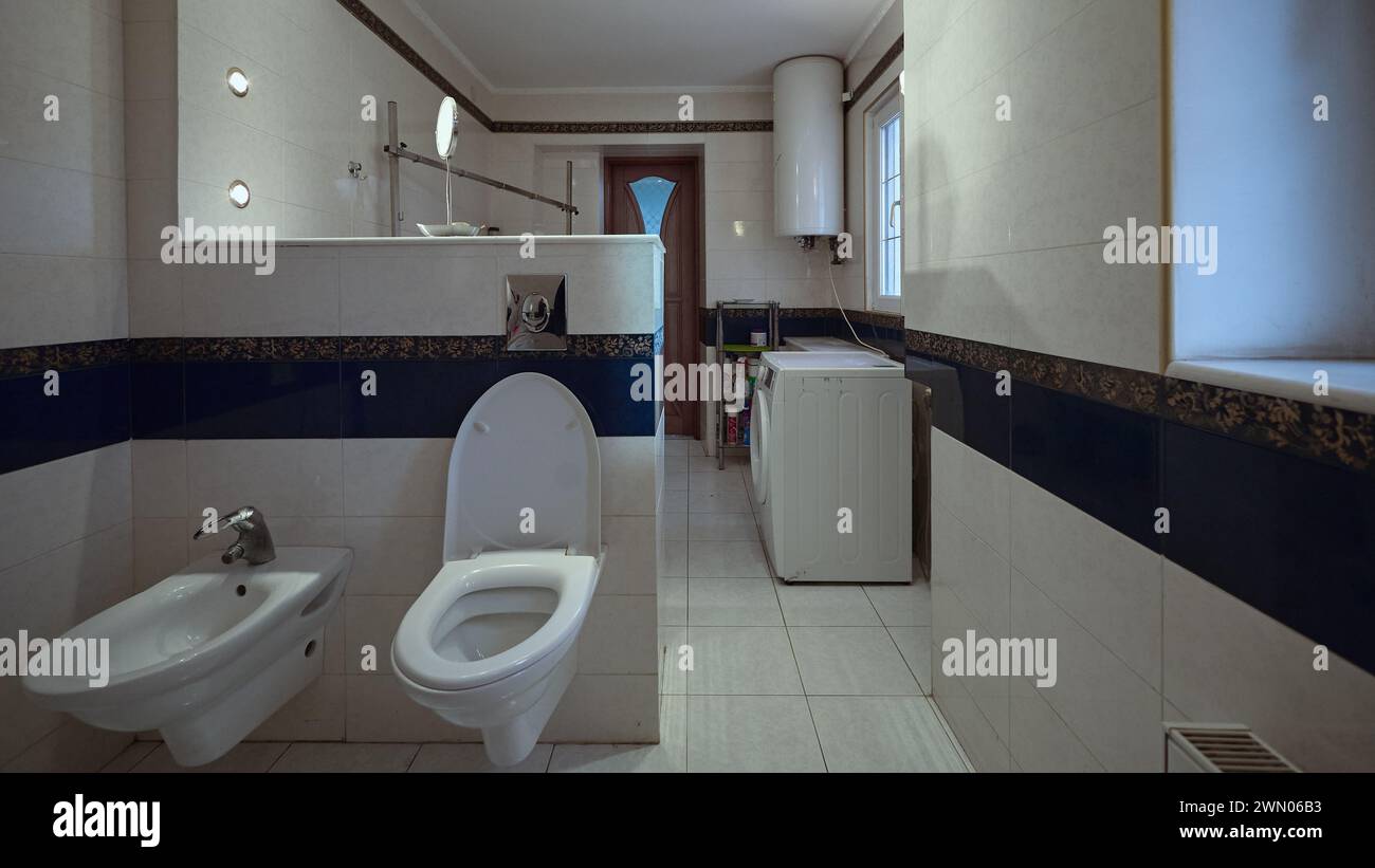 Bagno. Le pareti sono ricoperte di piastrelle di ceramica bianca, WC, bidet, lavatrice e caldaia ad acqua sul muro Foto Stock