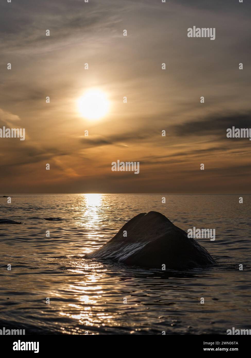 Nella tranquilla solitudine dei mari di Veczemju Klintis, una pietra solitaria si crogiola nel caldo bagliore del tramonto, invitanti momenti di introspezione e calma Foto Stock