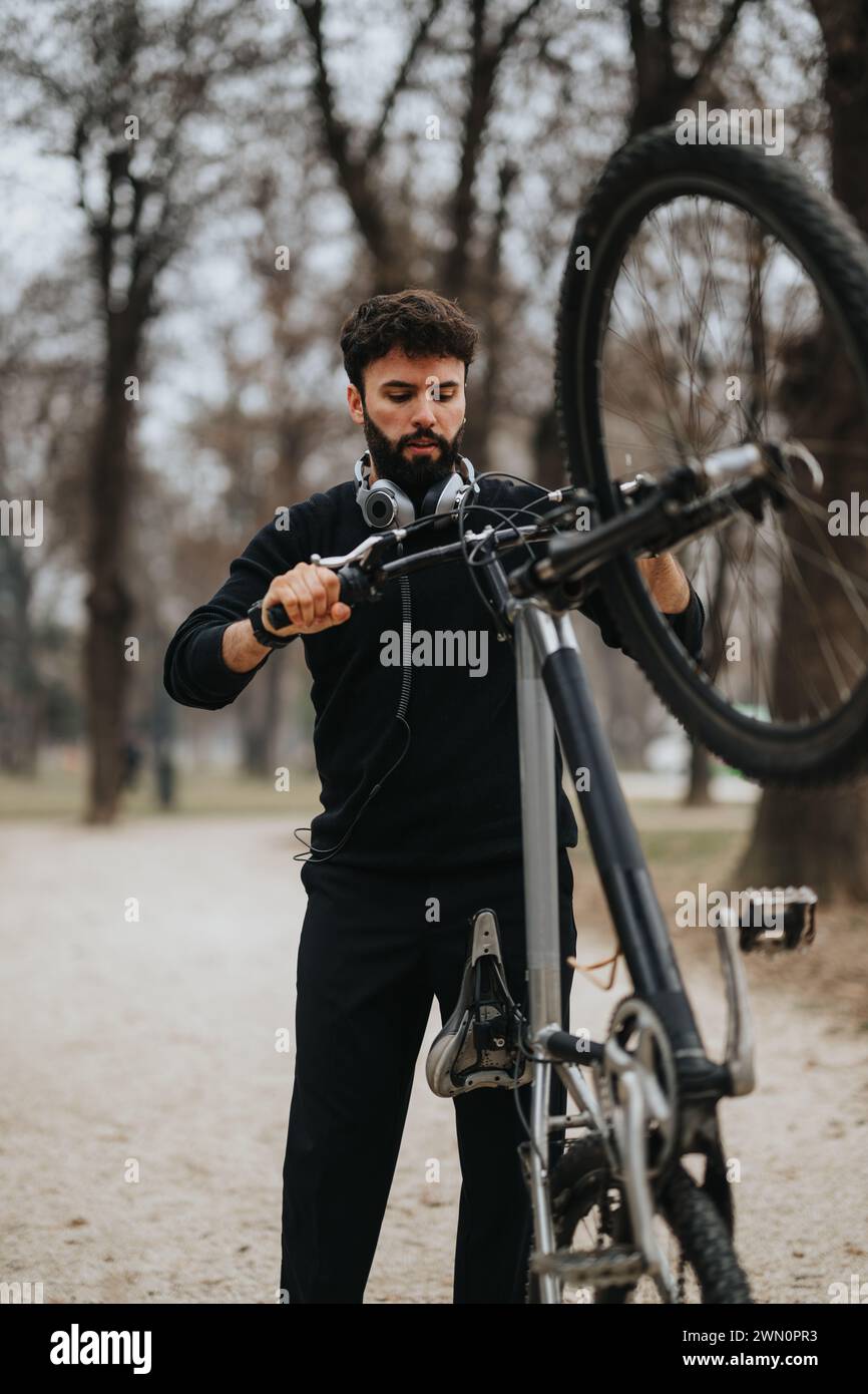 Uomo d'affari concentrato che mette a punto la sua bicicletta in un parco con le cuffie Foto Stock