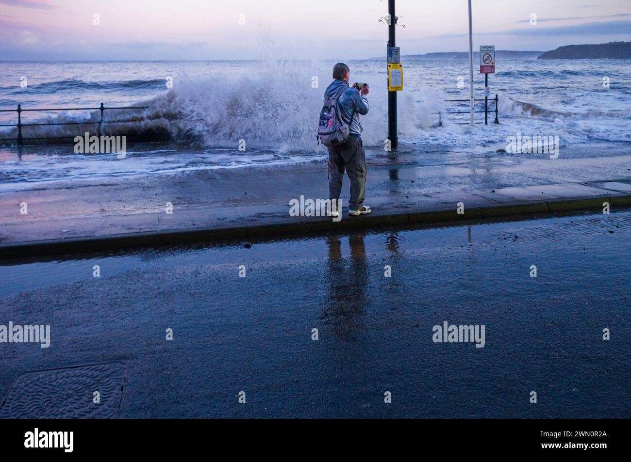 Un uomo molto bagnato che filma in alto mare a Scarborough sul suo cellulare Foto Stock