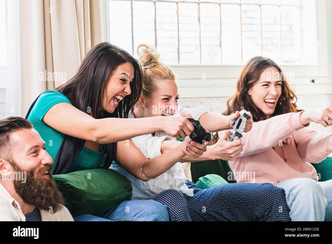 Un esuberante gruppo di amici viene colto in un momento di giocosa competizione, mentre si divertono in una vivace battaglia videoludica su un comodo divano Foto Stock