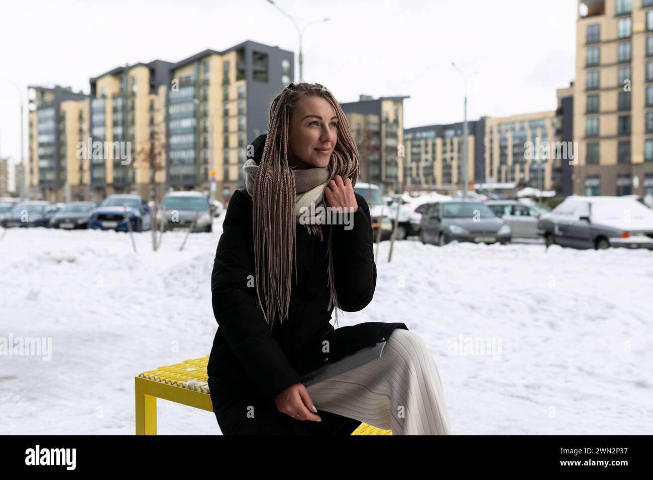 Una donna sorridente con dreadlock biondi cammina per la città con la neve in inverno Foto Stock