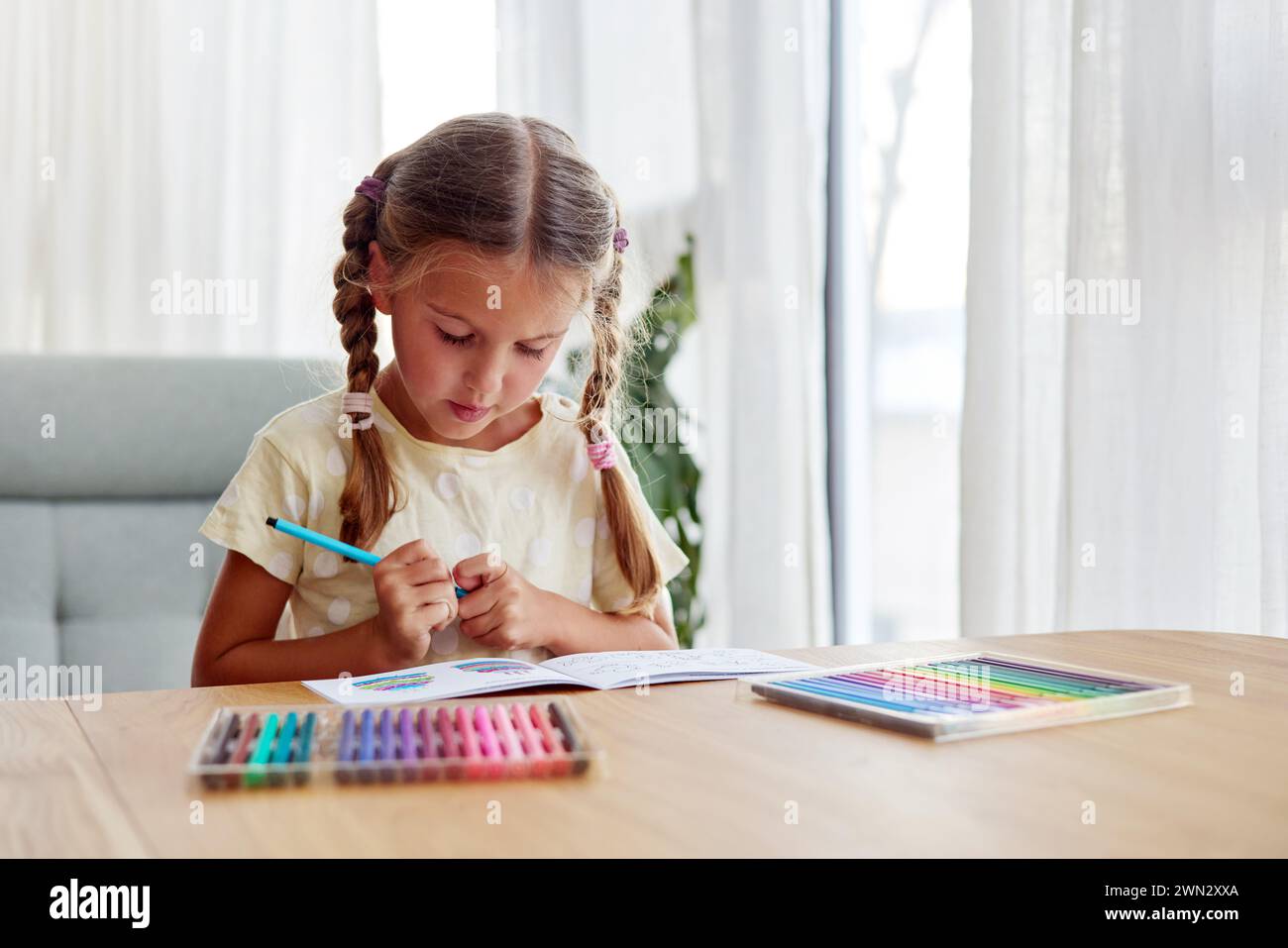 La ragazza con trecce sceglie una penna con punta in feltro brillante per disegnare l'immagine Foto Stock
