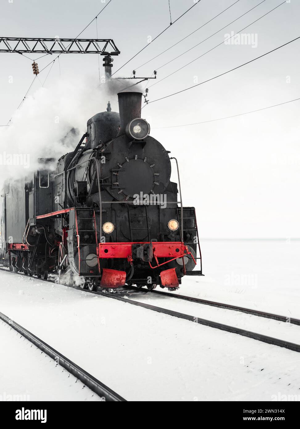 Vecchia locomotiva a vapore che passa in un campo innevato. Locomotiva nera d'epoca che tira un treno in un giorno d'inverno. Foto Stock