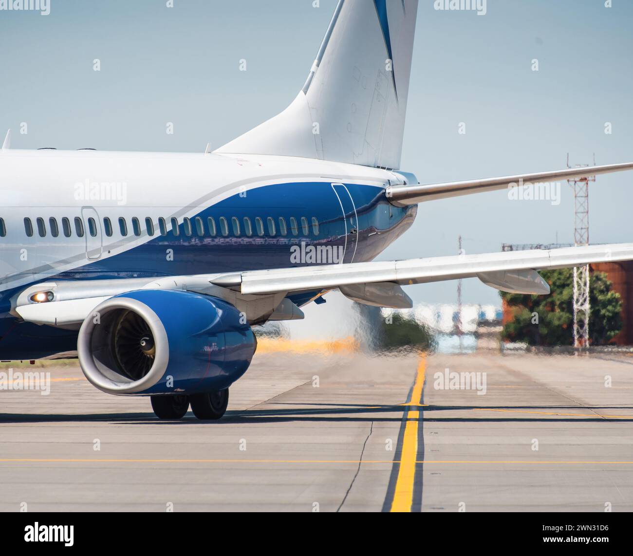Sezione posteriore di aerei passeggeri bianchi e blu in movimento sulla pista di rullaggio dell'aeroporto: Aria calda che fuoriesce dal retro del motore e distorce la vista. Foto Stock