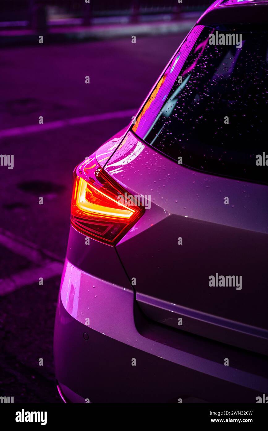 Luce di posizione posteriore del SEDILE Ibiza berlina. Immagine in primo piano verticale di un berretto compatto con luce viola. Riflesso delle luci della città nella carrozzeria delle vetture. Foto Stock