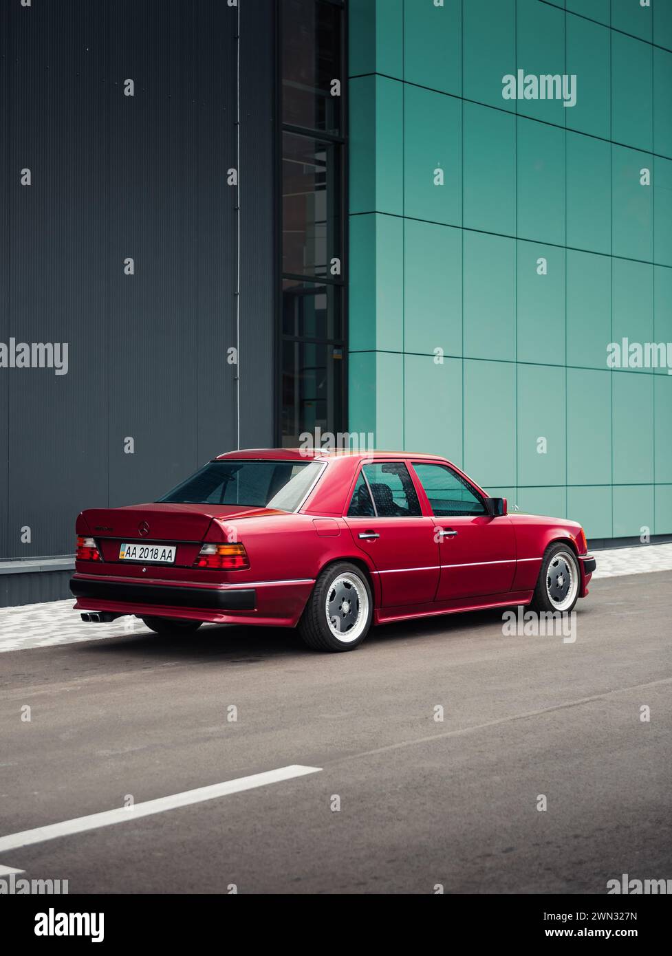 Vista posteriore di tre quarti di Mercedes-Benz 400E (W124) nel kit carrozzeria AMG davanti alla parete turchese. berlina tedesca degli anni '1980 parcheggiata vicino a un edificio moderno. Foto Stock