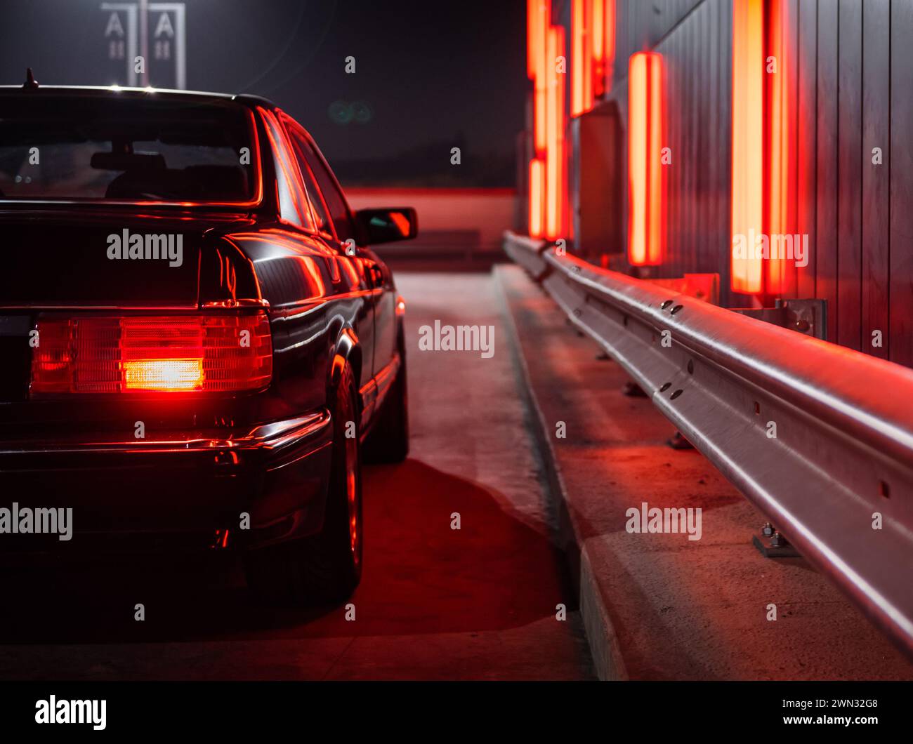 Mercedes Benz SEC coupé nera di notte vicino al muro al neon. Vista laterale del gruppo ottico posteriore della Mercedes 1980s con luci di posizione posteriori accese Foto Stock