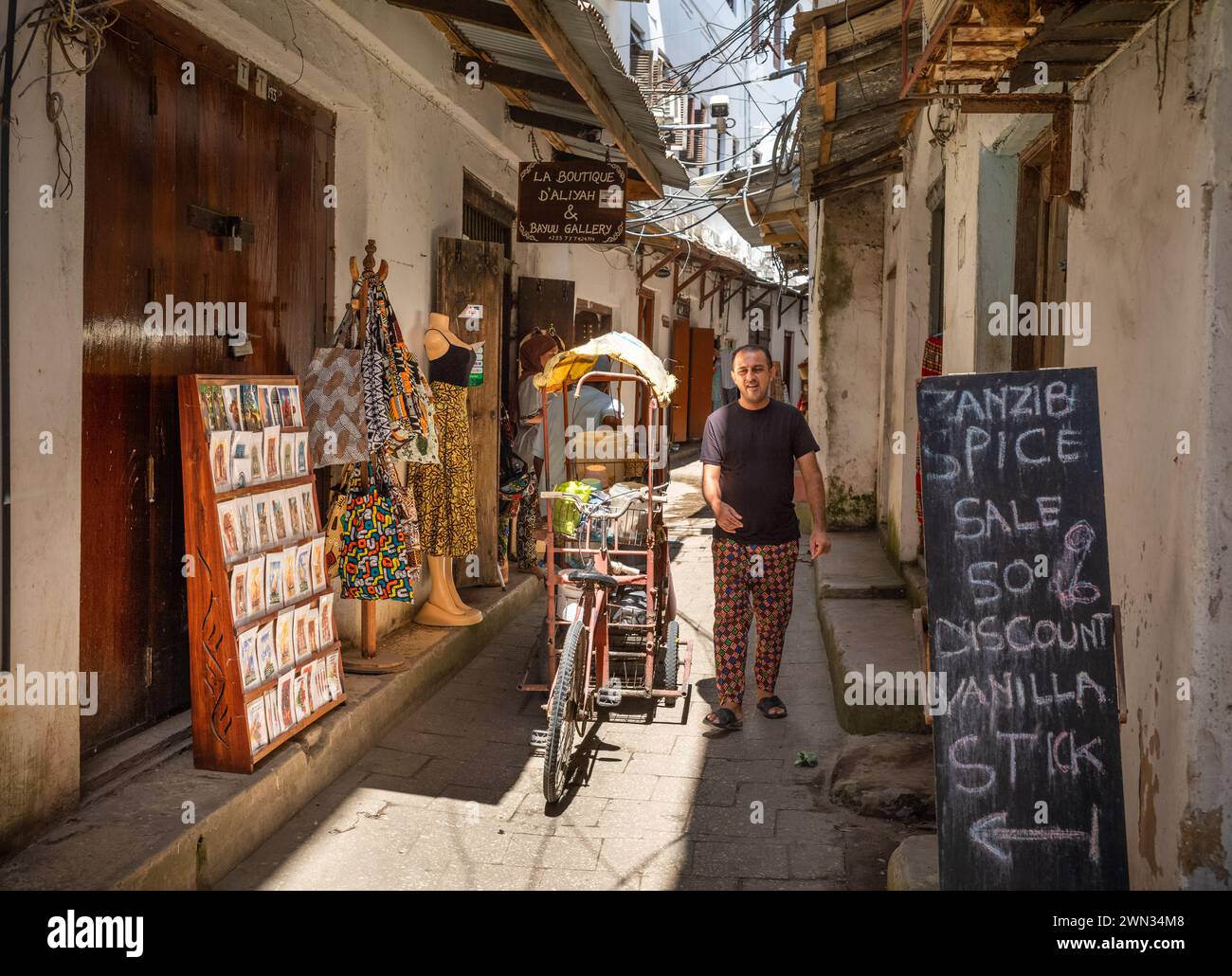 Un venditore di tè con il suo triciclo in un vicolo vicino a un negozio di spezie, Stone Town, Zanzibar, Tanzania Foto Stock