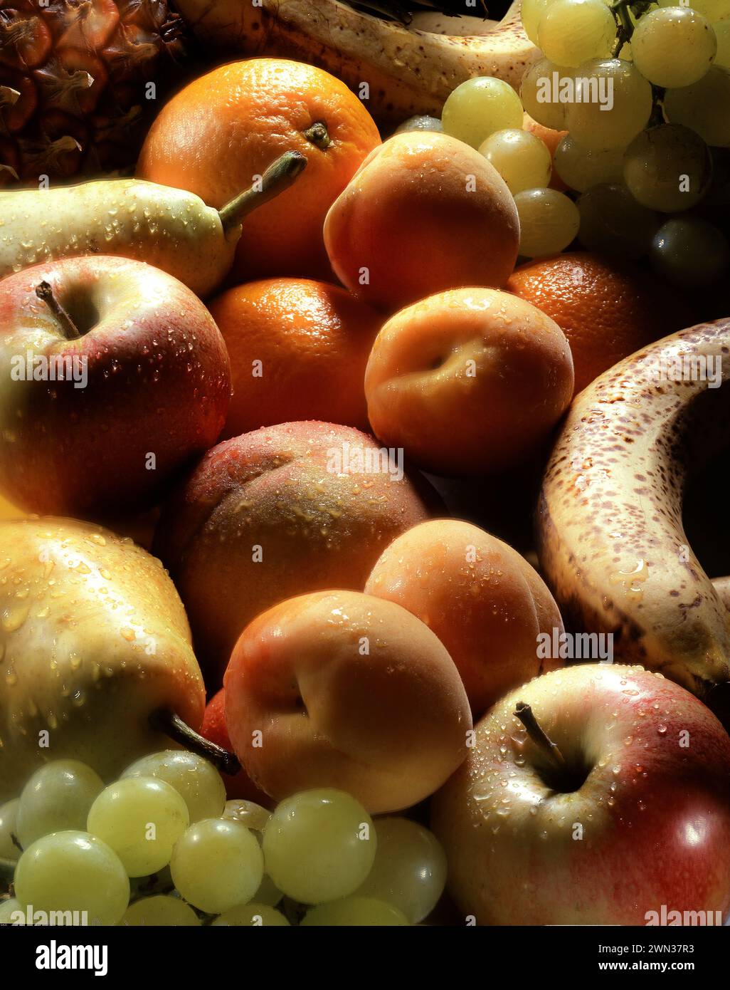 Un vivace assortimento di frutta fresca risplende di umidità: Mele, arance, albicocche, uva, banane, pere e molto altro ancora, immerse in una luce spettacolare. Foto Stock