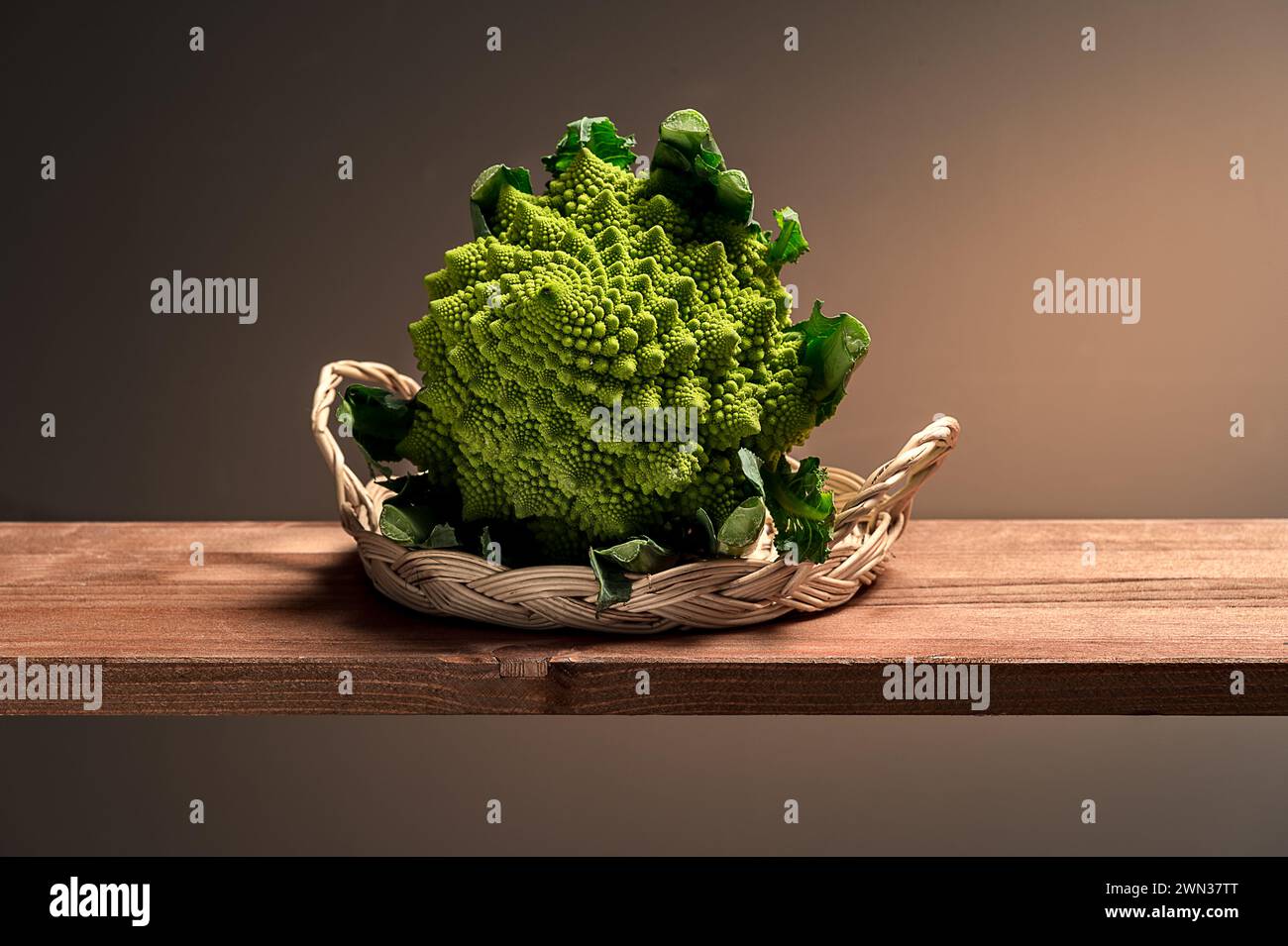 I broccoli Romanesco con frattali verdi vivaci si trovano in un cesto intrecciato su legno, che mescola la geometria della natura con fascino rustico e tonalità calde. Foto Stock