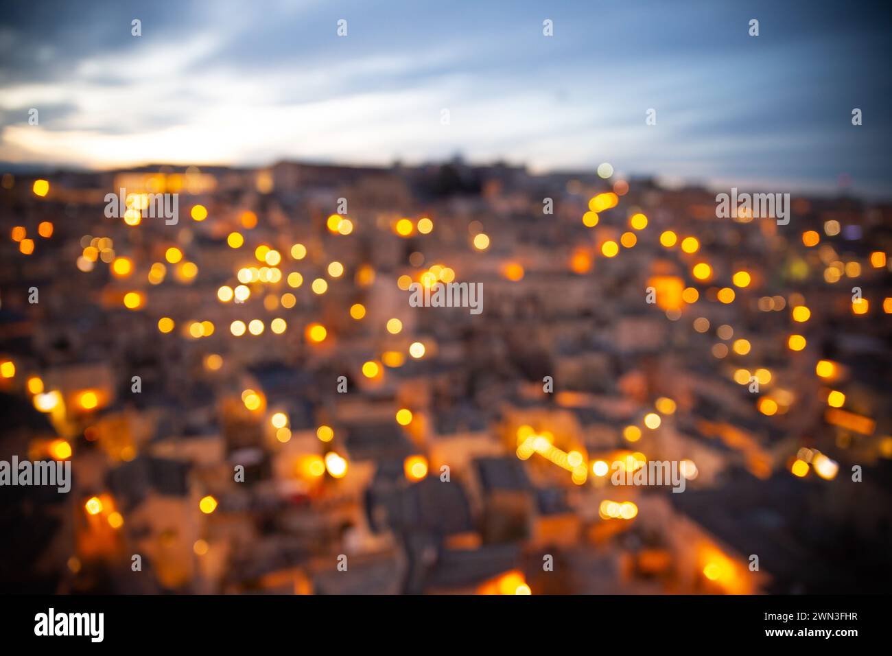 Vista ariale sfocata di Matera sassi al tramonto con illuminazione stradale accesa, Italia Foto Stock