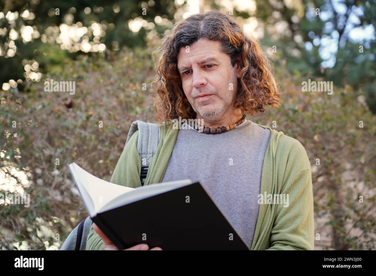professore universitario con zaino che lavora fuori a leggere un notebook. giornata mondiale del libro Foto Stock