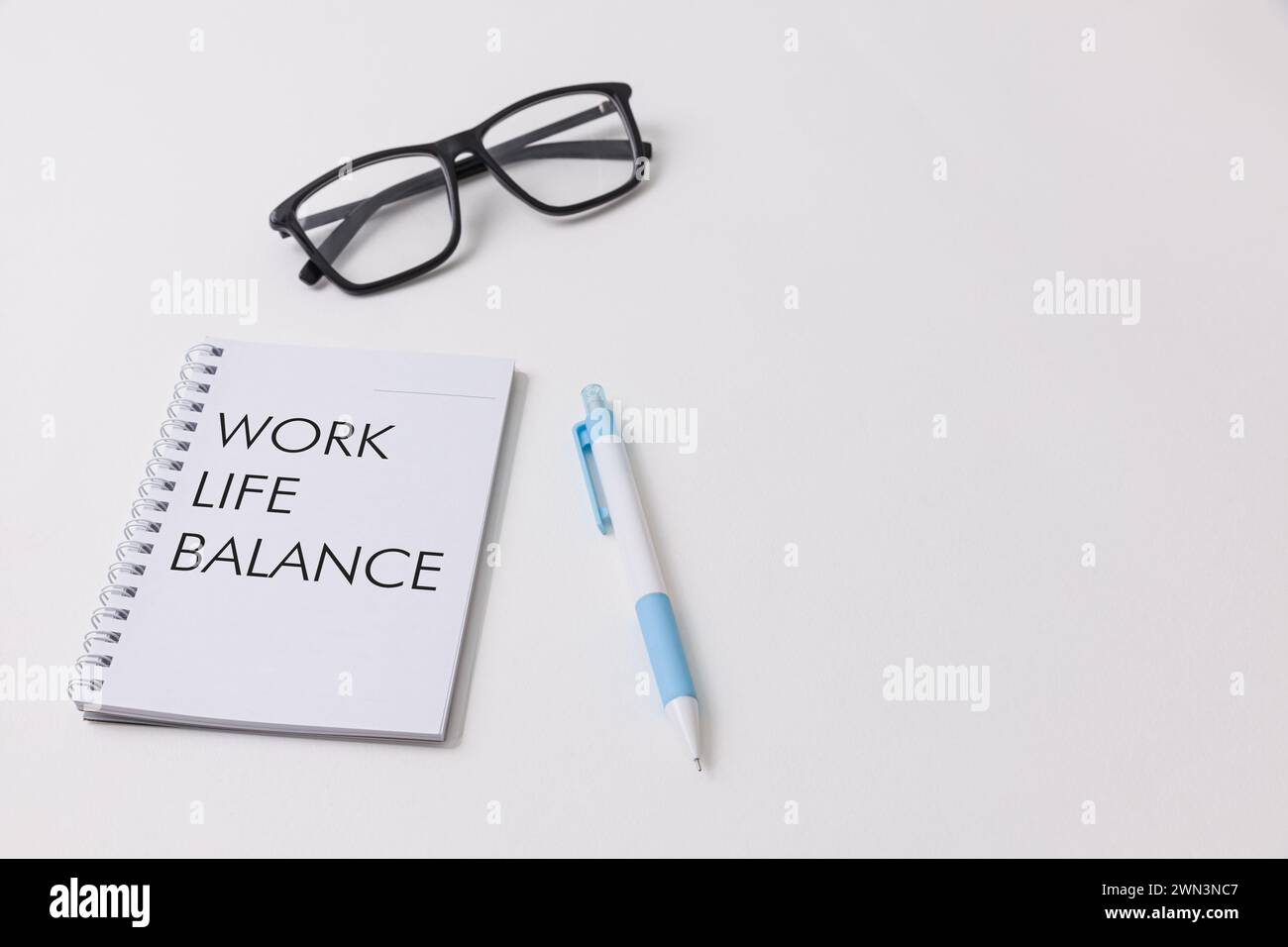 Una scrivania bianca che mostra un notebook con scritto un equilibrio di vita lavorativa, penna blu, occhiali neri che simboleggiano le opportunità di lavoro e l'ambiente di lavoro dell'ufficio Foto Stock