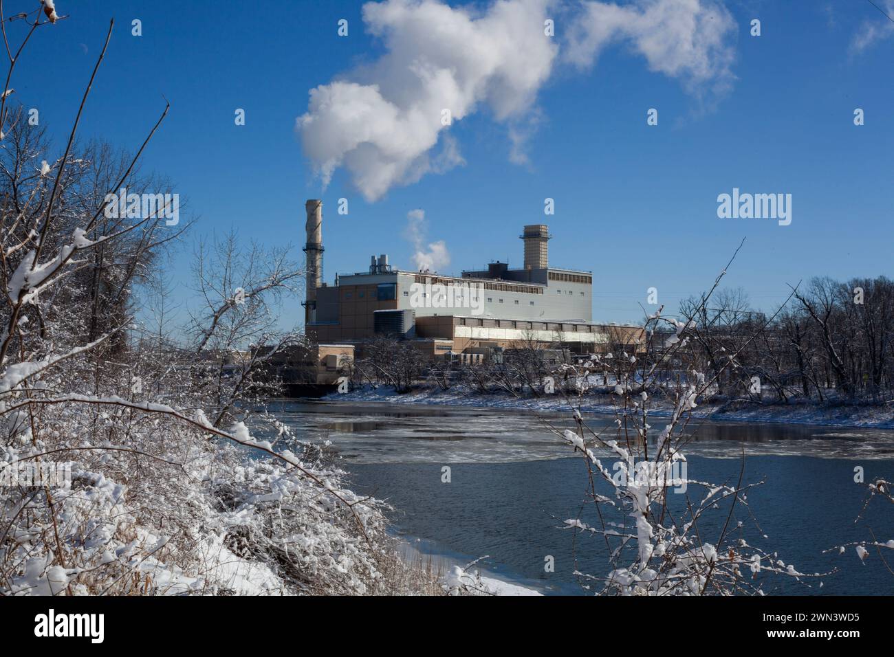 Impianto industriale che emette vapore su un fiume innevato Foto Stock